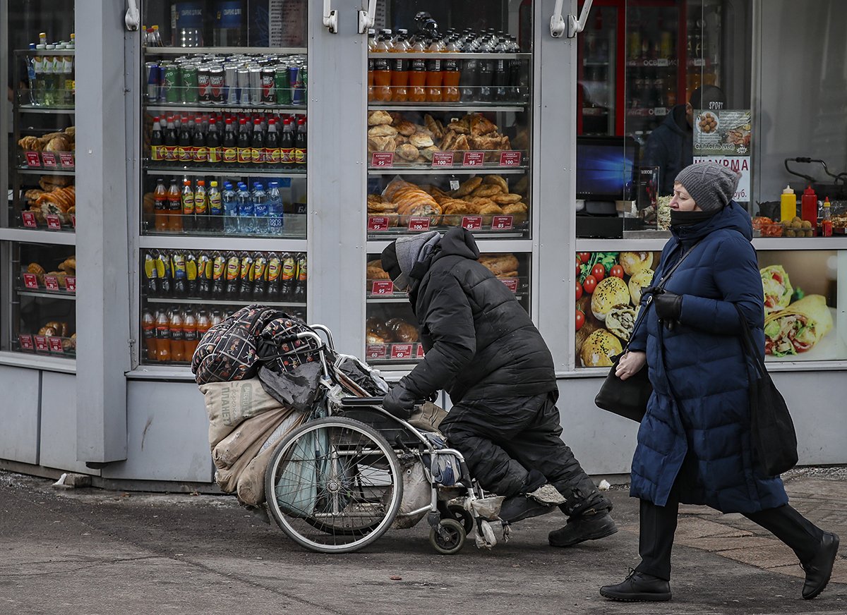 Бездомный мужчина толкает инвалидную коляску со своими вещами перед витриной магазина в Москве, Россия. Фото:Юрий Кочетков / EPA-EFE