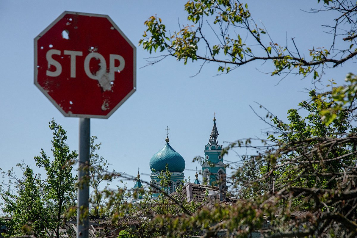 Разрушенный храм на фоне обстрелянного дорожного знака в Козинке, май 2024 года